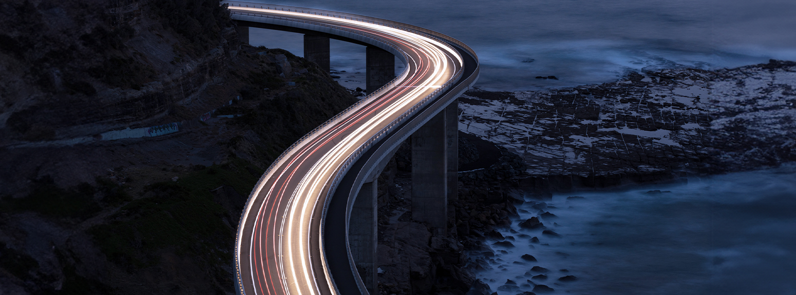 Scie luminose di auto che passano su un ponte lungo il mare