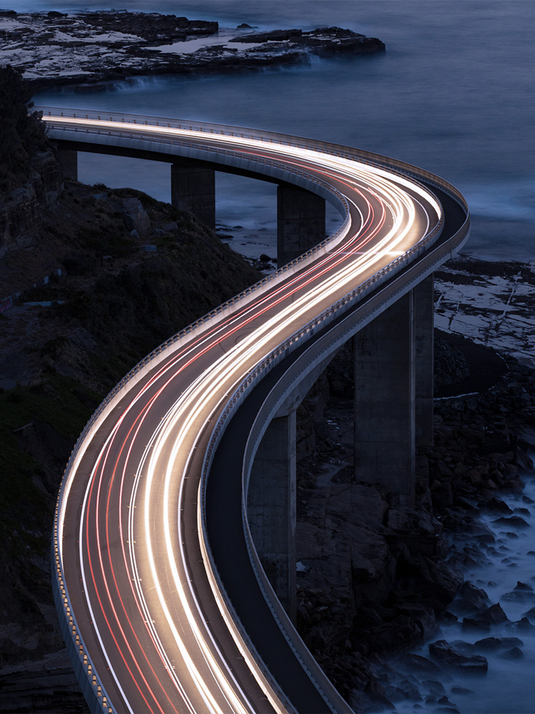 Scie luminose di auto che passano su un ponte lungo il mare
