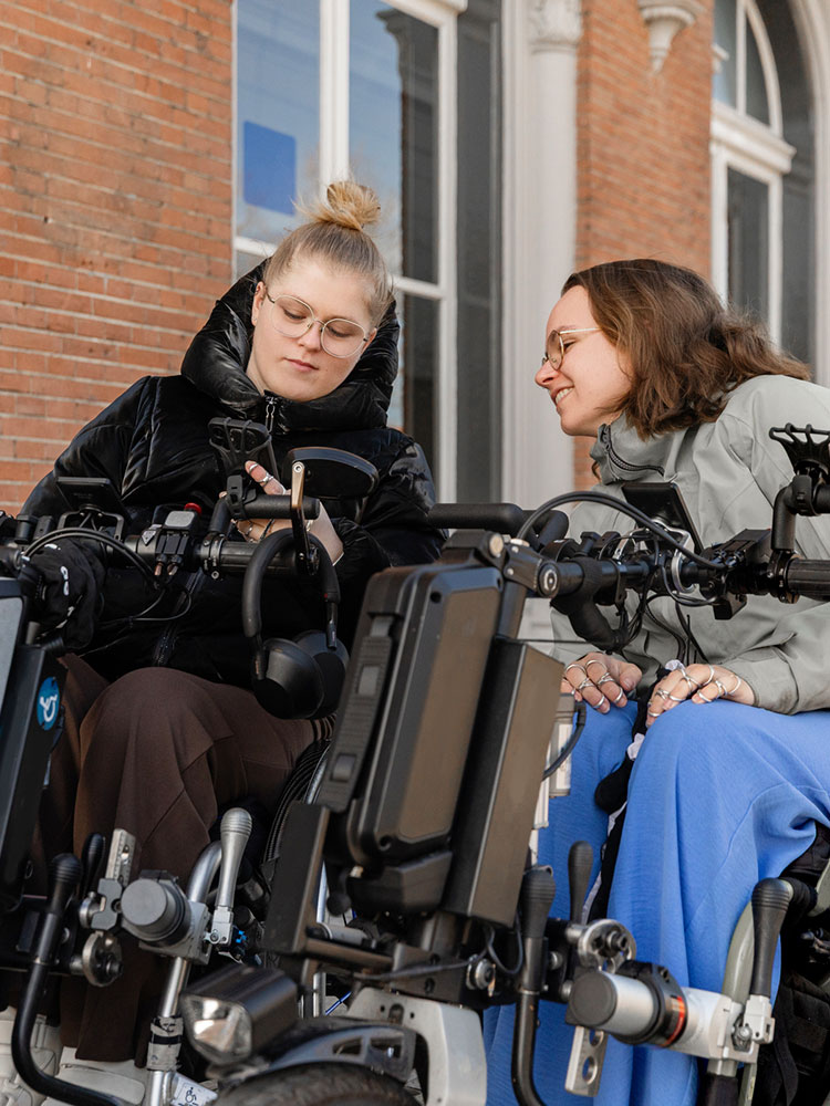 due donne disabili usano cellulare sedute su sedia a rotelle